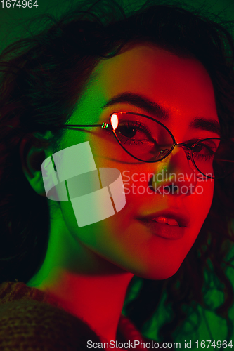 Image of Caucasian woman\'s portrait isolated on green studio background in multicolored neon light