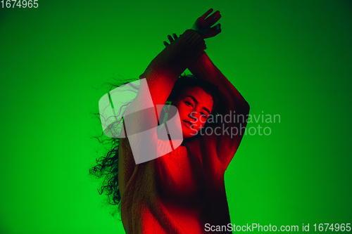 Image of Caucasian woman\'s portrait isolated on green studio background in multicolored neon light