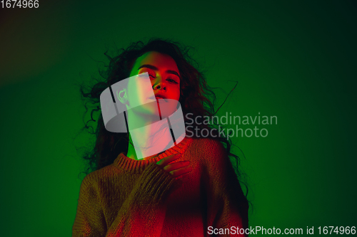 Image of Caucasian woman\'s portrait isolated on green studio background in multicolored neon light