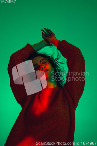 Image of Caucasian woman\'s portrait isolated on green studio background in multicolored neon light