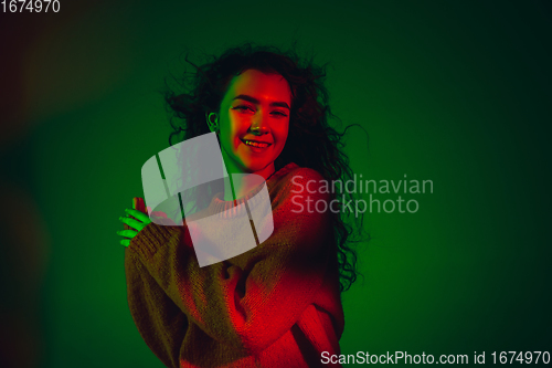 Image of Caucasian woman\'s portrait isolated on green studio background in multicolored neon light