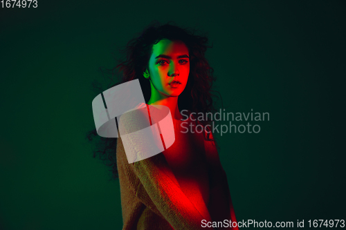 Image of Caucasian woman\'s portrait isolated on green studio background in multicolored neon light