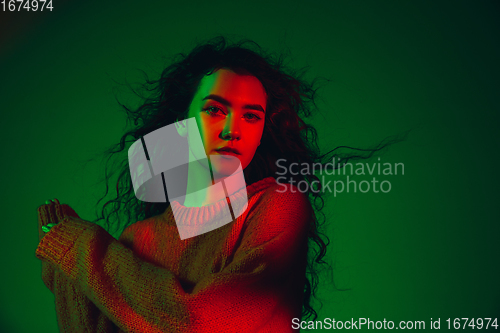 Image of Caucasian woman\'s portrait isolated on green studio background in multicolored neon light