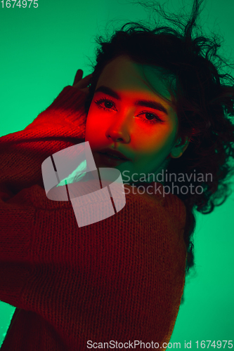 Image of Caucasian woman\'s portrait isolated on green studio background in multicolored neon light