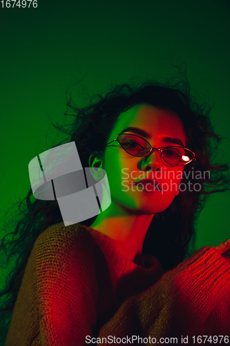 Image of Caucasian woman\'s portrait isolated on green studio background in multicolored neon light