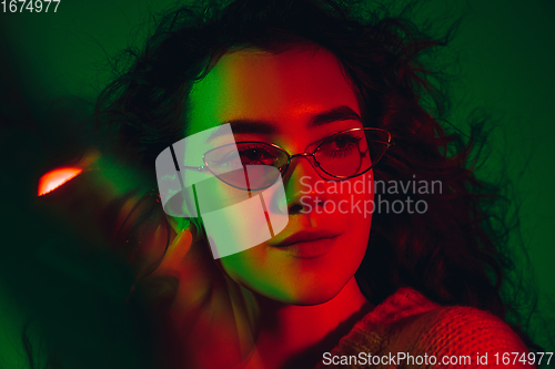 Image of Caucasian woman\'s portrait isolated on green studio background in multicolored neon light