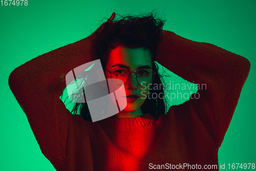 Image of Caucasian woman\'s portrait isolated on green studio background in multicolored neon light