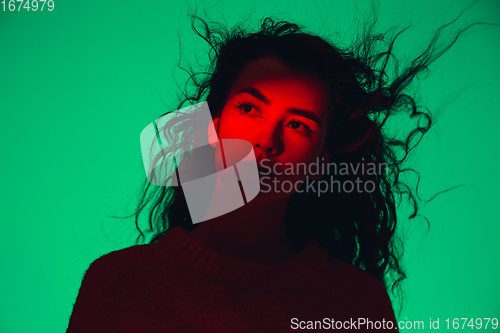 Image of Caucasian woman\'s portrait isolated on green studio background in multicolored neon light