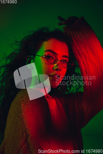 Image of Caucasian woman\'s portrait isolated on green studio background in multicolored neon light