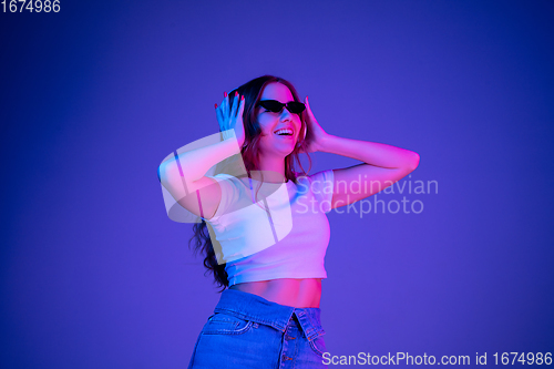 Image of Caucasian woman\'s portrait isolated on blue studio background in multicolored neon light