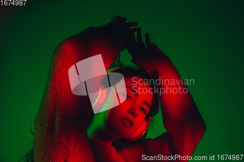 Image of Caucasian woman\'s portrait isolated on green studio background in multicolored neon light