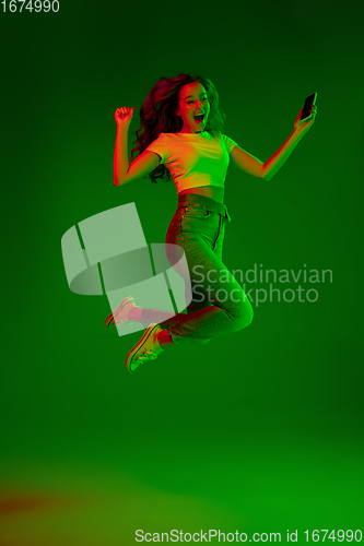 Image of Caucasian woman\'s portrait isolated on green studio background in multicolored neon light