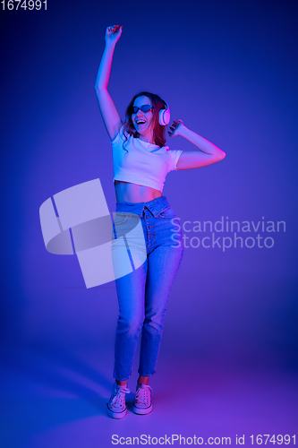 Image of Caucasian woman\'s portrait isolated on blue studio background in multicolored neon light