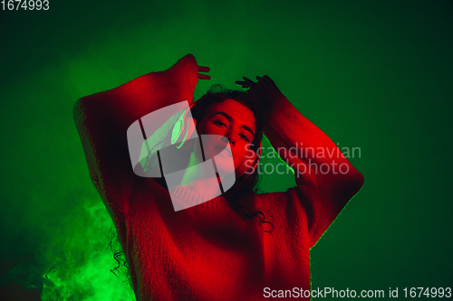 Image of Caucasian woman\'s portrait isolated on green studio background in multicolored neon light