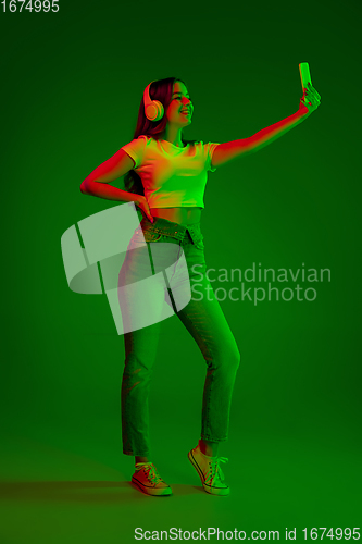 Image of Caucasian woman\'s portrait isolated on green studio background in multicolored neon light