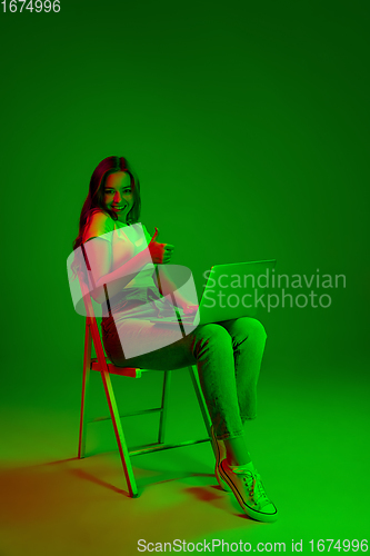 Image of Caucasian woman\'s portrait isolated on green studio background in multicolored neon light