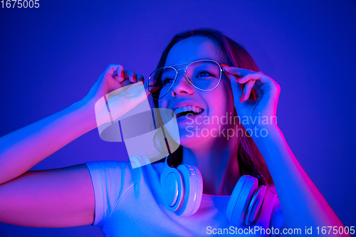 Image of Caucasian woman\'s portrait isolated on blue studio background in multicolored neon light