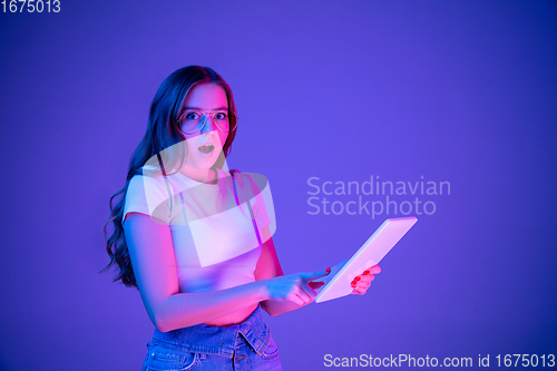 Image of Caucasian woman\'s portrait isolated on blue studio background in multicolored neon light