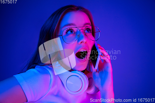 Image of Caucasian woman\'s portrait isolated on blue studio background in multicolored neon light