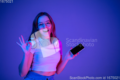 Image of Caucasian woman\'s portrait isolated on blue studio background in multicolored neon light