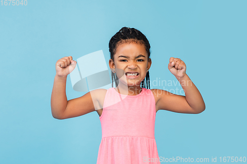 Image of Happy longhair brunette little girl isolated on blue studio background. Looks happy, cheerful, sincere. Copyspace. Childhood, education, emotions concept