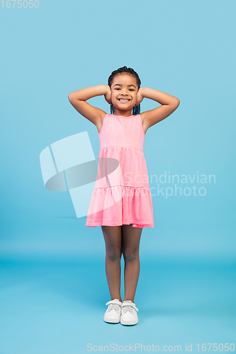 Image of Happy longhair brunette little girl isolated on blue studio background. Looks happy, cheerful, sincere. Copyspace. Childhood, education, emotions concept