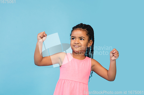 Image of Happy longhair brunette little girl isolated on blue studio background. Looks happy, cheerful, sincere. Copyspace. Childhood, education, emotions concept