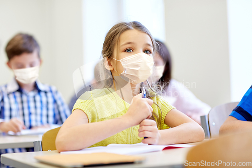 Image of little student girl in mask on lesson at school