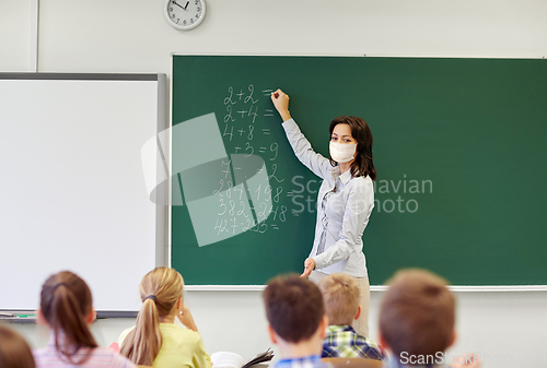 Image of teacher in mask writing on chalkboard at school