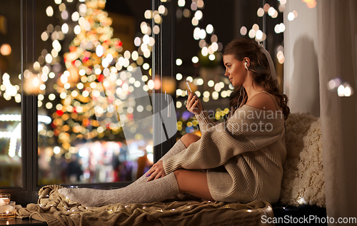 Image of woman with smartphone and earphones on christmas