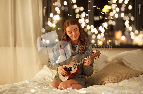 Image of happy young woman playing guitar in bed at home