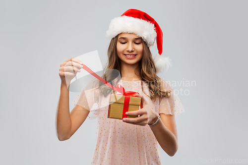 Image of teenage girl in santa hat opening christmas gift
