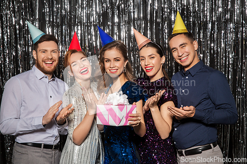 Image of happy friends in party hats with birthday gift