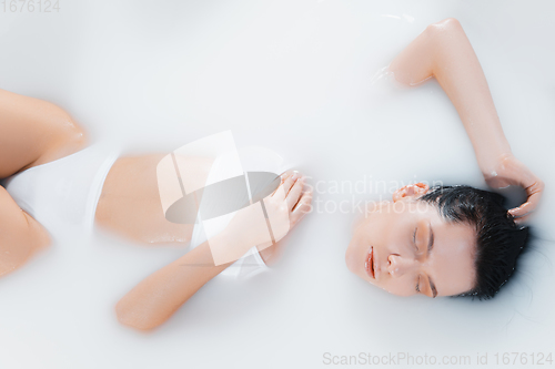 Image of Beautiful female model in the milk bath with soft white glowing. Copyspace for advertising. Beauty, fashion, style, bodycare concept.