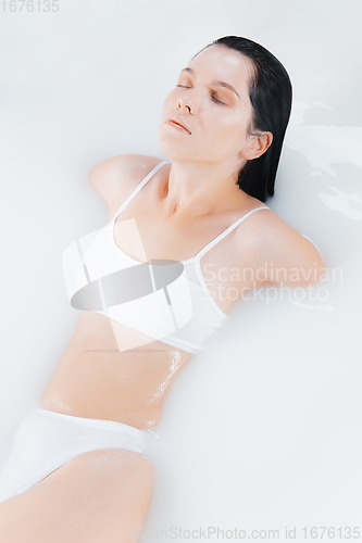 Image of Beautiful female model in the milk bath with soft white glowing. Copyspace for advertising. Beauty, fashion, style, bodycare concept.