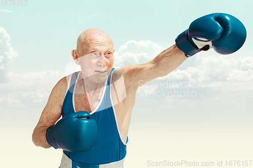 Image of Senior man wearing sportwear boxing on sky background. Concept of sport, activity, movement, wellbeing. Copyspace, ad.