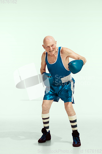 Image of Senior man wearing sportwear boxing isolated on studio background. Concept of sport, activity, movement, wellbeing. Copyspace, ad.