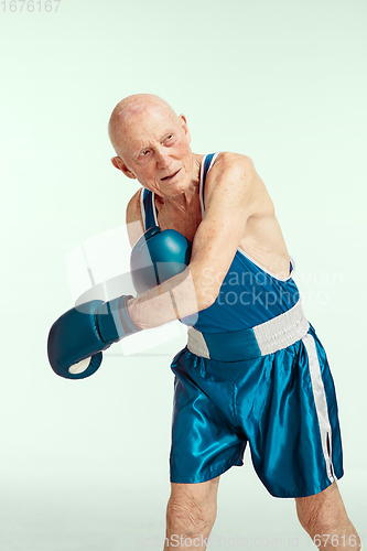 Image of Senior man wearing sportwear boxing isolated on studio background. Concept of sport, activity, movement, wellbeing. Copyspace, ad.