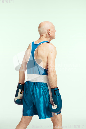 Image of Senior man wearing sportwear boxing isolated on studio background. Concept of sport, activity, movement, wellbeing. Copyspace, ad.