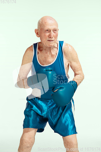 Image of Senior man wearing sportwear boxing isolated on studio background. Concept of sport, activity, movement, wellbeing. Copyspace, ad.