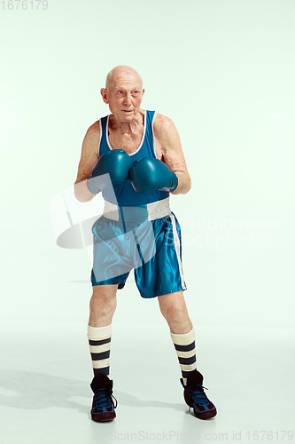 Image of Senior man wearing sportwear boxing isolated on studio background. Concept of sport, activity, movement, wellbeing. Copyspace, ad.