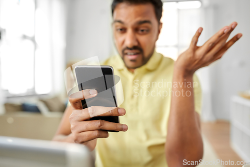 Image of angry indian man with smartphone working at home