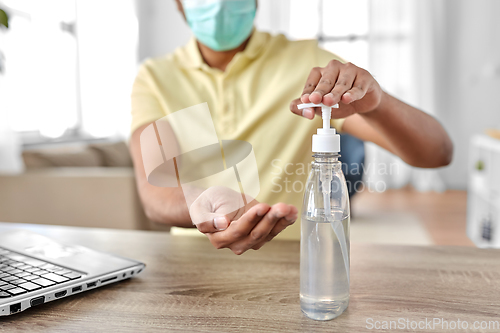 Image of man in mask using hand sanitizer at home office