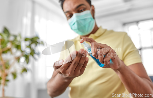 Image of close up of man in mask applying hand sanitizer