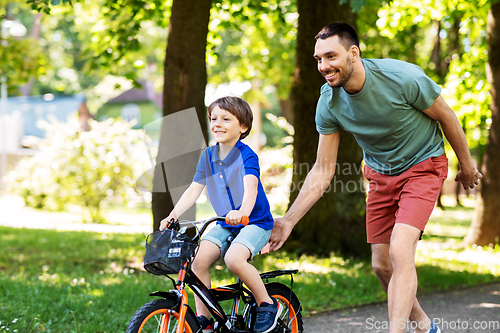 Image of father teaching little son to ride bicycle at park