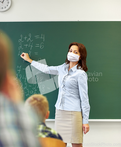 Image of teacher in mask writing on chalkboard at school