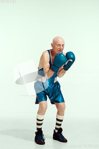 Image of Senior man wearing sportwear boxing isolated on studio background. Concept of sport, activity, movement, wellbeing. Copyspace, ad.