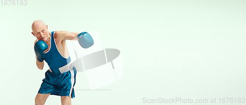 Image of Senior man wearing sportwear boxing isolated on studio background. Concept of sport, activity, movement, wellbeing. Copyspace, ad.