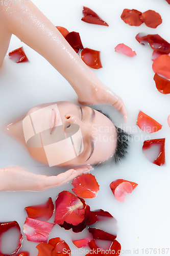 Image of Close up female face in the milk bath with soft white glowing and rose petals. Copyspace for advertising. Beauty, fashion, style, bodycare concept.