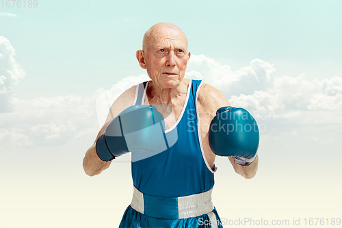 Image of Senior man wearing sportwear boxing on sky background. Concept of sport, activity, movement, wellbeing. Copyspace, ad.